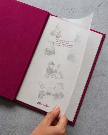 Una mano solleva il foglio trasparente stampato in rosso sopra le illustrazioni del menu